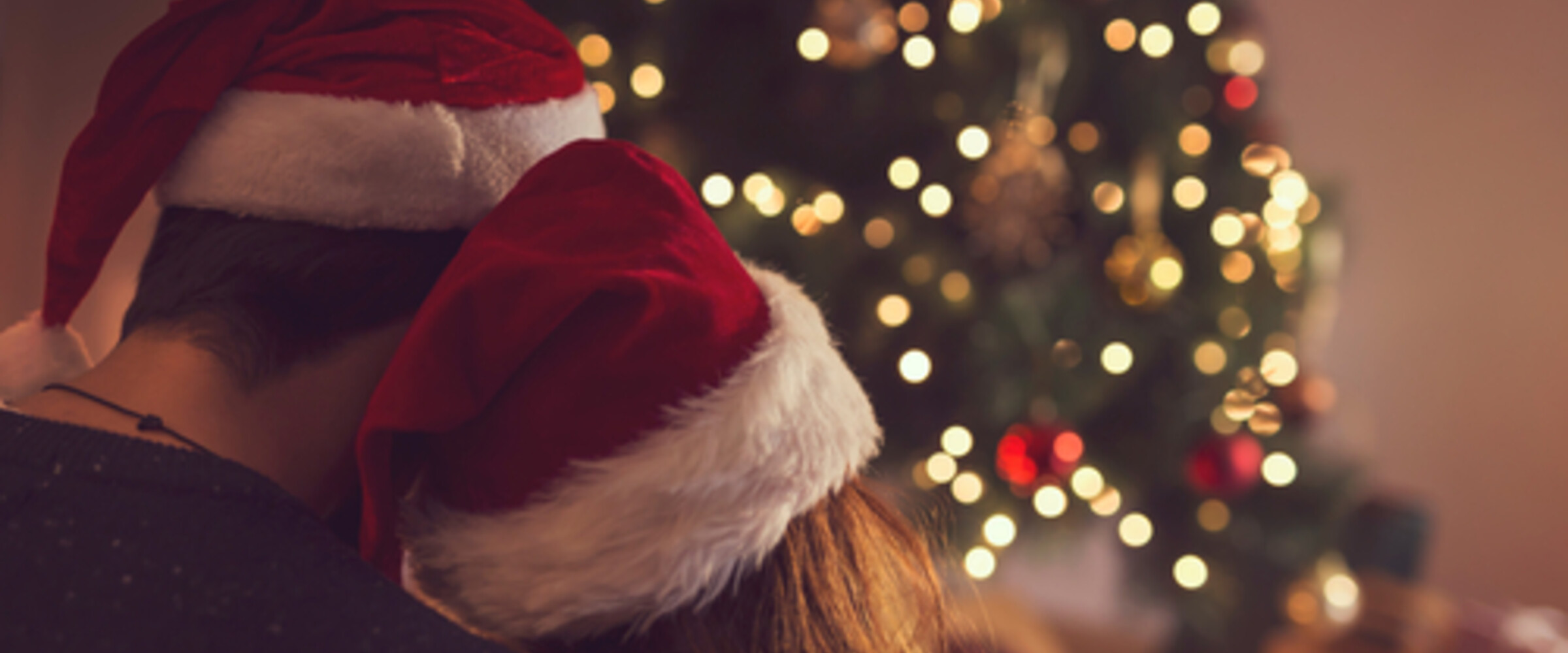 couple cuddling in front of christmas tree